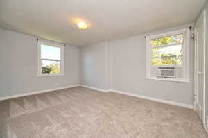 Empty room with cooling unit, a textured ceiling, and carpet flooring