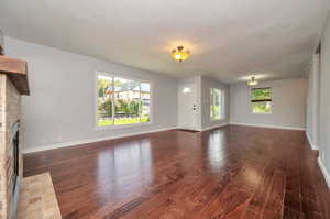 Unfurnished living room with a fireplace, dark wood-type flooring, and plenty of natural light