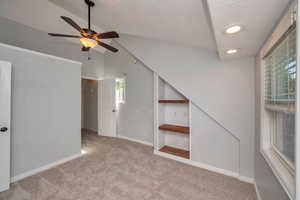 Carpeted spare room featuring vaulted ceiling, ceiling fan, plenty of natural light, and a textured ceiling