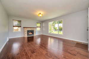 Unfurnished living room with dark wood-type flooring and a stone fireplace