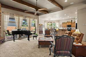 Living room featuring ceiling fan with notable chandelier, beam ceiling, and light colored carpet