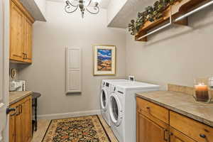 Laundry area featuring an inviting chandelier, light tile patterned floors, cabinets, and independent washer and dryer