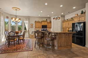 Kitchen featuring a kitchen breakfast bar, black appliances, a kitchen island with sink, and a notable chandelier