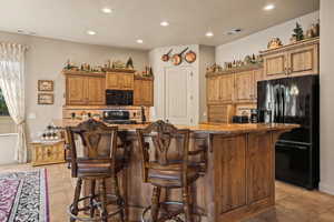 Kitchen with a kitchen breakfast bar, black appliances, backsplash, and an island with sink