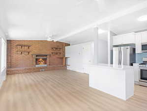 Unfurnished living room featuring light hardwood / wood-style floors, a brick fireplace, vaulted ceiling with beams, ceiling fan, and brick wall