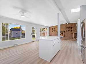 Kitchen with light hardwood / wood-style floors, white cabinets, a kitchen island, a fireplace, and brick wall