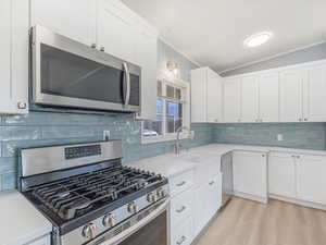 Kitchen with white cabinets, ornamental molding, sink, tasteful backsplash, and appliances with stainless steel finishes