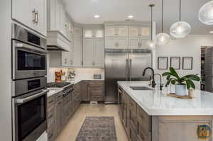 Kitchen with a spacious island, stainless steel appliances, light stone counters, and sink