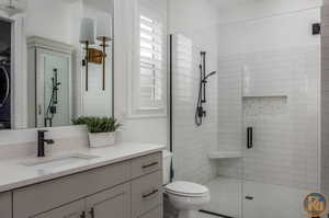 Bathroom featuring a shower with shower door, stacked washer / dryer, vanity, and toilet