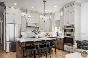 Kitchen with tasteful backsplash, a kitchen island, stainless steel appliances, light wood-type flooring, and decorative light fixtures