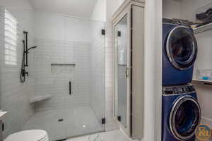 Bathroom with stacked washer and clothes dryer, a shower with door, and toilet