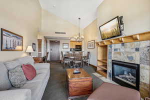 Carpeted living room featuring a fireplace, a chandelier, and high vaulted ceiling