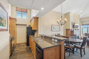 Kitchen featuring kitchen peninsula, black appliances, decorative light fixtures, dark stone counters, and sink