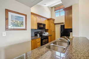 Kitchen with black appliances, dark stone countertops, sink, and tasteful backsplash