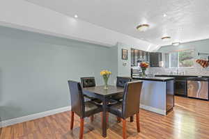 Dining room with a textured ceiling, lofted ceiling, sink, and light hardwood / wood-style flooring