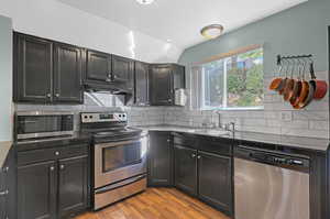 Kitchen with appliances with stainless steel finishes, sink, lofted ceiling, and decorative backsplash