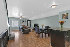 Dining room featuring vaulted ceiling, ceiling fan, dark wood-type flooring, and a textured ceiling