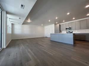 Kitchen featuring a wealth of natural light, dark wood-type flooring, an island with sink, gray cabinetry, and appliances with stainless steel finishes