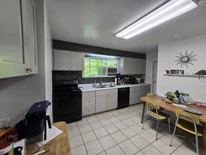 Kitchen with tasteful backsplash, sink, gray cabinetry, black appliances, and light tile patterned floors