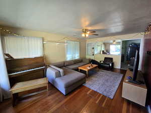 Living room with ceiling fan and dark wood-type flooring