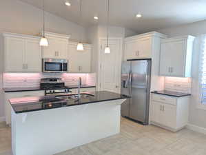 Kitchen featuring stainless steel appliances, lofted ceiling, a center island with sink, and white cabinets