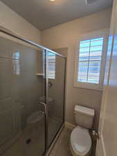 Bathroom with a shower with door, tile patterned floors, and toilet