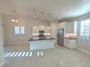 Kitchen with a kitchen island with sink, stainless steel appliances, vaulted ceiling, decorative light fixtures, and white cabinets