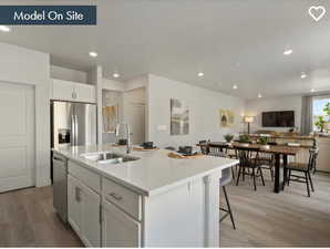 Kitchen featuring light wood-type flooring, sink, an island with sink, white cabinets, and appliances with stainless steel finishes