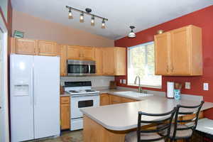 Kitchen with light brown cabinets, sink, kitchen peninsula, new appliances, and vaulted ceiling