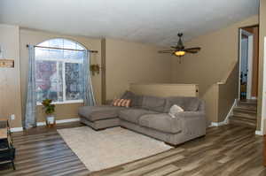 Living room with a textured ceiling, lofted ceiling, new LVP flooring, and ceiling fan