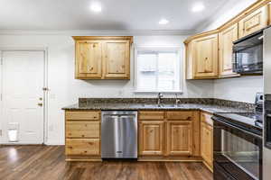 Kitchen with sink, dark hardwood / wood-style floors, dark stone countertops, black appliances, and ornamental molding