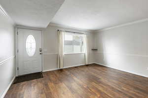 Entryway with ornamental molding, a textured ceiling, and dark wood-type flooring