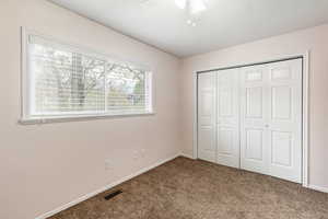 Unfurnished bedroom featuring multiple windows, ceiling fan, a closet, and carpet