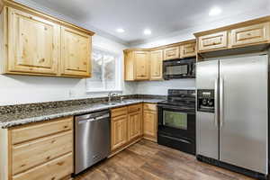 Kitchen with light brown cabinetry, dark hardwood / wood-style flooring, crown molding, sink, and black appliances