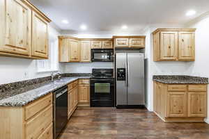 Kitchen with dark wood-type flooring, dark stone counters, black appliances, sink, and light brown cabinetry