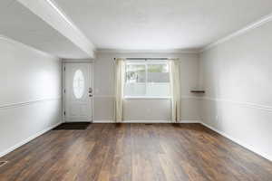 Foyer entrance with a textured ceiling, dark hardwood / wood-style floors, and ornamental molding