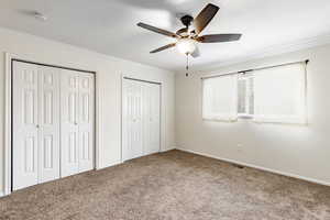 Unfurnished bedroom featuring carpet, two closets, ceiling fan, and crown molding