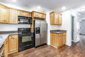 Kitchen featuring dark stone counters, black appliances, ornamental molding, light brown cabinetry, and dark hardwood / wood-style flooring