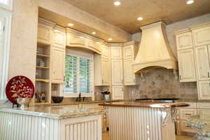 Kitchen with cream cabinets, premium range hood, light stone countertops, and kitchen peninsula