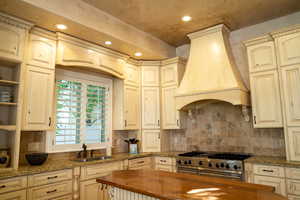 Kitchen featuring custom exhaust hood, sink, wooden counters, high end stainless steel range, and decorative backsplash