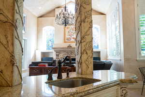 Kitchen with light stone counters, sink, a chandelier, and vaulted ceiling