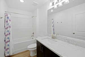 Full bathroom with shower / tub combo, hardwood / wood-style flooring, vanity, and toilet