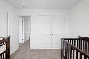 Bedroom featuring light carpet, a closet, and a nursery area