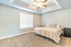 Carpeted bedroom with ceiling fan and a raised ceiling