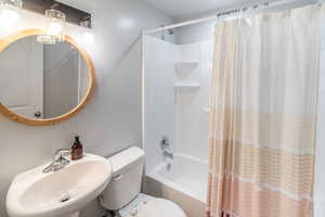 Full bathroom with toilet, sink, and shower / bathtub combination with curtain