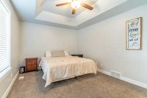 Bedroom with ceiling fan, a raised ceiling, and carpet flooring