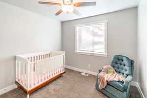 Carpeted bedroom with ceiling fan and a crib