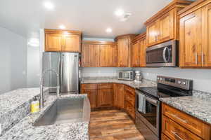 Kitchen with appliances with stainless steel finishes, sink, light stone counters, and hardwood / wood-style flooring