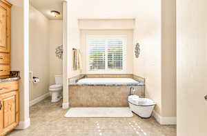 Bathroom featuring vanity, a relaxing tiled tub, toilet, and tile patterned floors