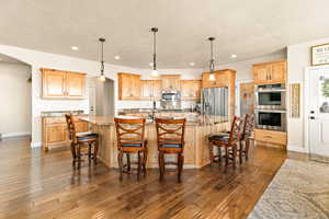 Kitchen featuring light stone countertops, stainless steel appliances, dark hardwood / wood-style floors, and a kitchen island with sink